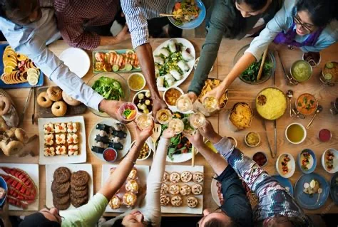 a long table seen from above, covered in shared dishes, hands reaching in